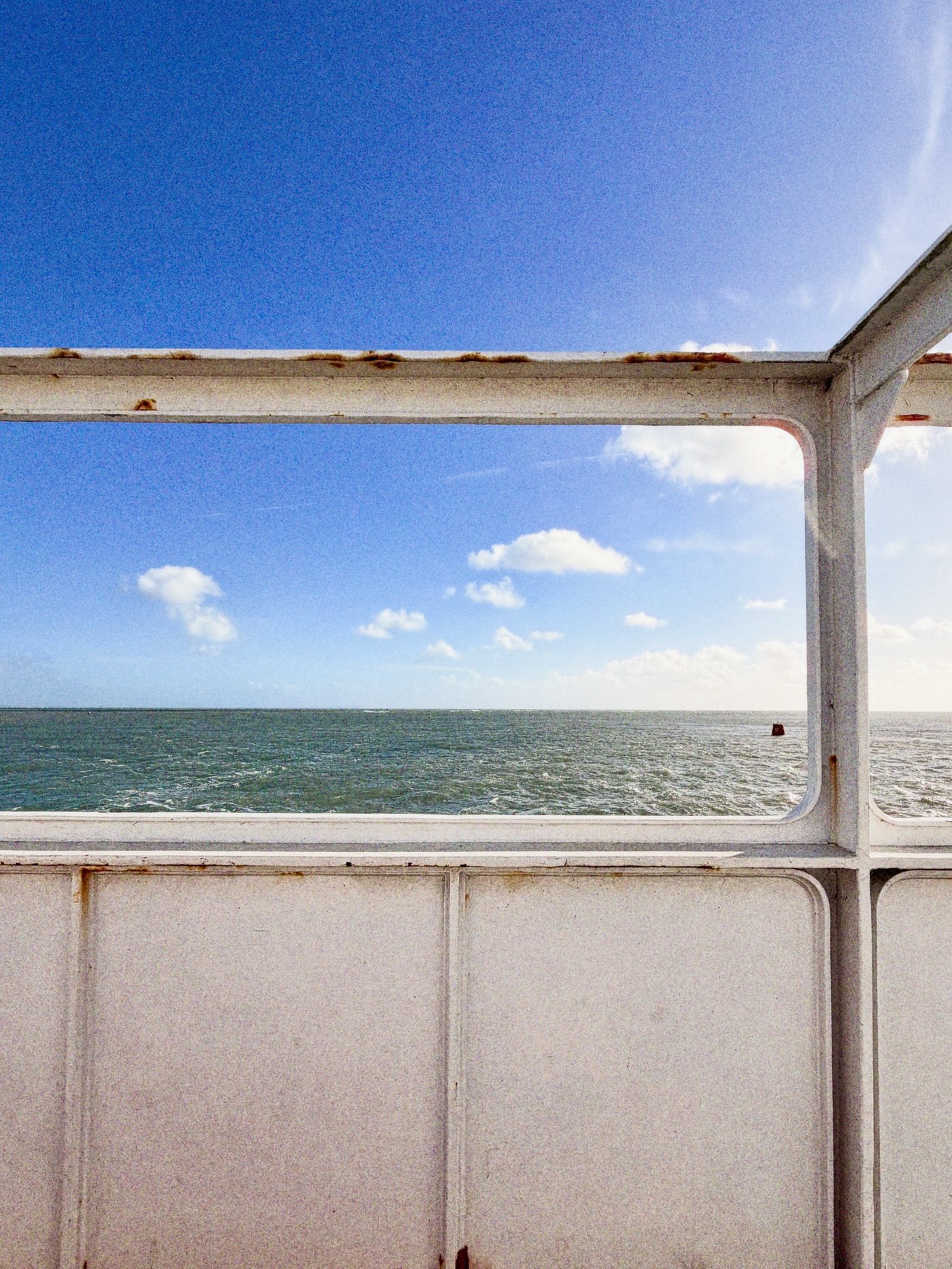 Blue sky and a calm sea framed by the white railings on the deck of a ferry